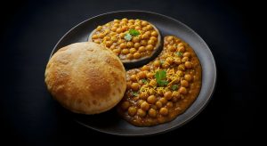 Chana bhatura served on a black plate, with spicy chickpea curry garnished with coriander and sev, alongside a fluffy deep-fried bread indian food recipes