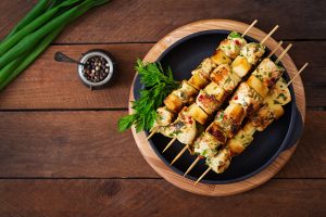 Grilled chicken skewers with apples and herbs on a black plate, garnished with parsley.